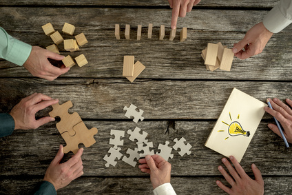 Businessmen planning business strategy while holding puzzle pieces, creating ideas with light bulb drawn on paper and rearranging wooden blocks. Conceptual of teamwork, strategy, vision or education.